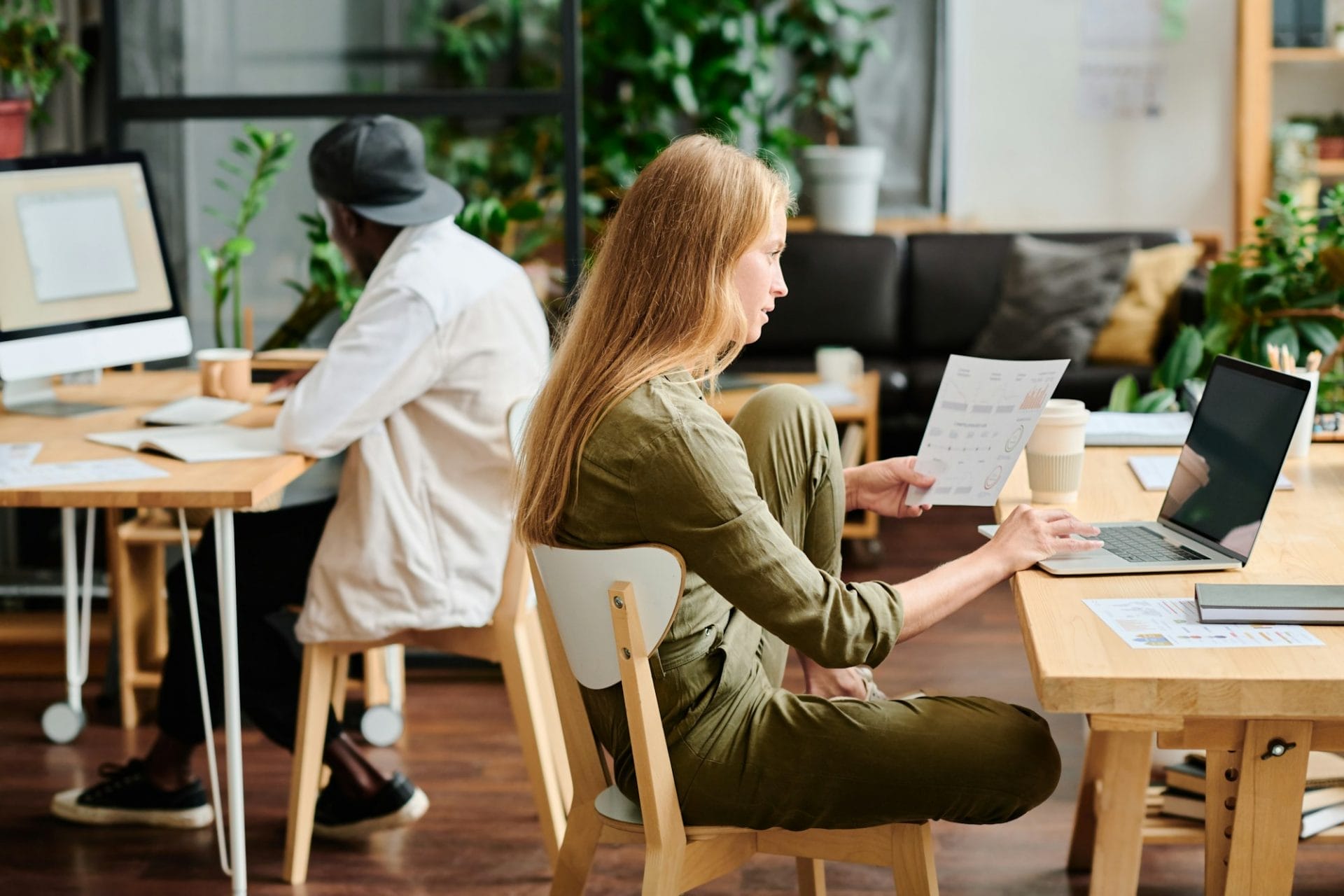 Young businesswoman with document looking at laptop screen by workplace